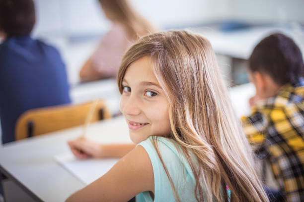 istock School girl writing on paper in classroom. 1312423406
