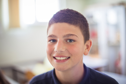 Portrait of smiling school boy in classroom. Focus is on foreground. Looking at camera.