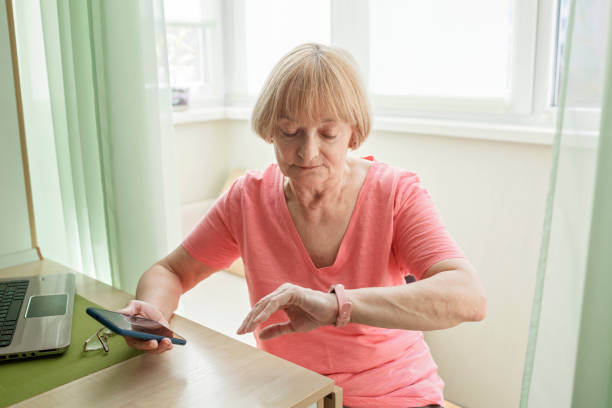 старшая женщина, проверяя информацию о здоровье с помощью смарт-часов, современного здравоохранения и поддержки - pulse clock стоковые фото и изображения
