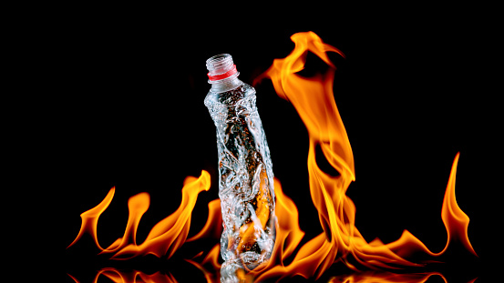 Close-up of plastic bottle melting by fire against black background.
