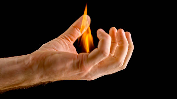 Close-up of man's hand holding flame in his hand against black background.