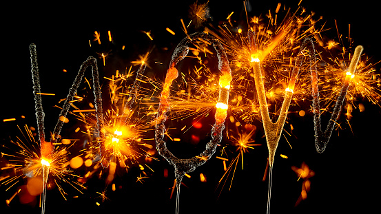Close-up of sparklers shaped to present the word 'WOW' burning and emitting sparks against black background.