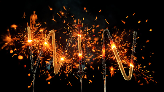 Close-up of sparklers shaped to present the word 'WIN' burning and emitting sparks against black background.