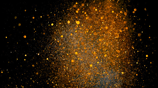Close-up of gold coloured glitter powder exploding on black background.