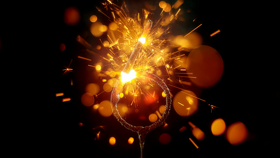 Close-up of sparkler in shape of 'NUMBER 6' emitting sparks while burning against black background.