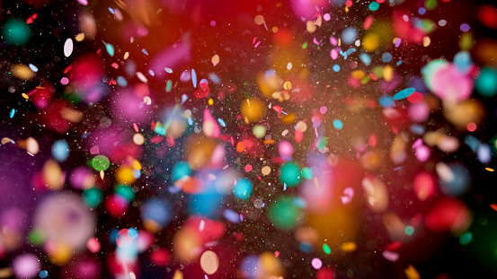Close-up of multi coloured confetti flying mid-air against black background.