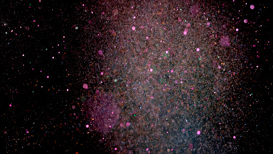 Close-up of pink coloured confetti flying mid-air against black background.