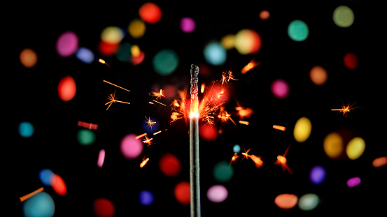 Close-up of sparkler emitting sparks while confetti falling against black background.