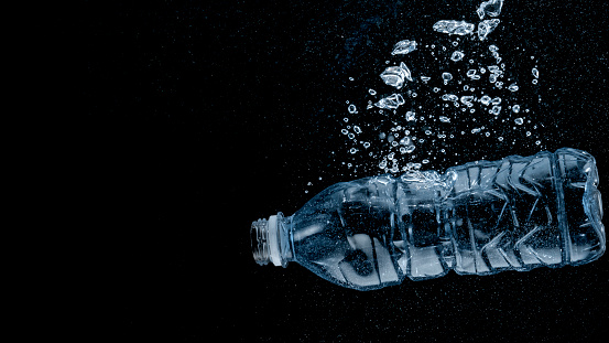 Plastic bottle without cap sinking in water against black background.