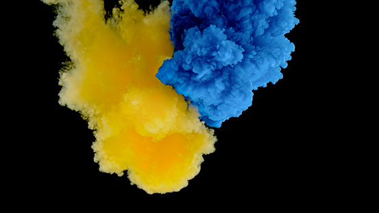 Close-up of yellow and blue colour ink drop falling into water against black background.