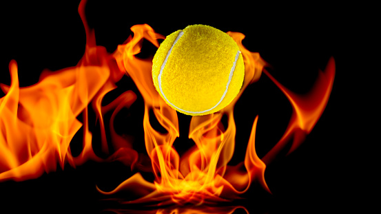 Close-up of tennis ball in flames against black background.