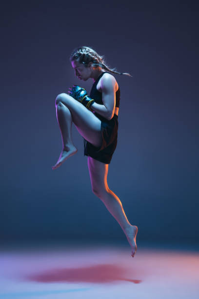 istock Caucasian female MMA fighter training isolated on blue background in neon light 1312431464