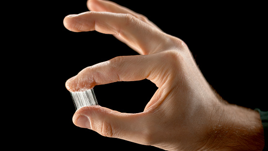 Close-up of man freeing two fingers stuck together by glue against black background.