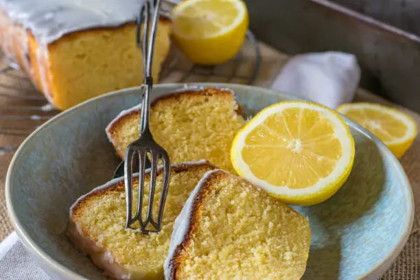 fresh and homemade baked lemon cake served sliced on a plate with rustic cake tong from above