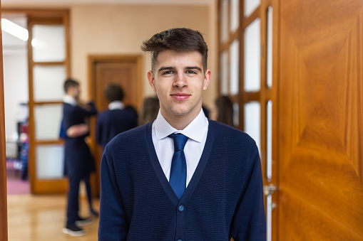 Back to school. Portrait of high school male student in front of the classroom. Other students standing behind him