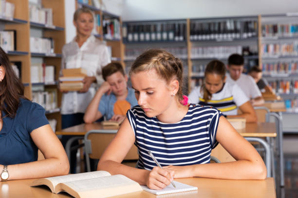 istock Schoolgirl writing lesson in classroom, teacher on background 1312439246