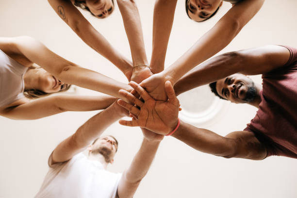 A group of young sporty people is putting their hands together. They are laughing and enjoying themselves. Horizontal daylight photo from worm's eye view.