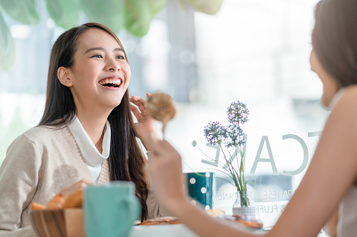 attractive asian female talking good positive conversation to friends with smiling laugh and happiness moment at counter near window at cafe with daylight from garden positive attitude relationship
