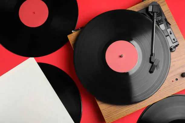 Photo of Modern player and vinyl records on red background, flat lay