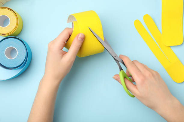 istock Woman cutting bright kinesio tape at light blue table, top view 1312441491