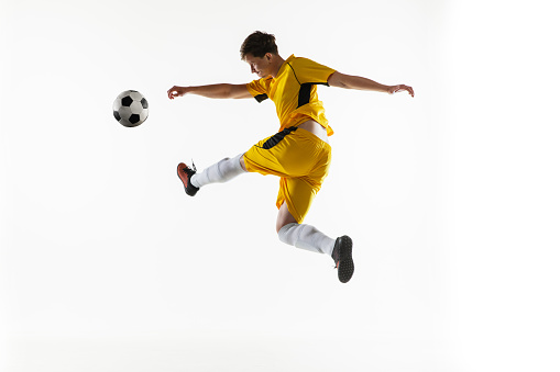 Kick football ball. One Caucasian man, male soccer football player in yellow uniform training isolated on white background. Concept of action, team sport game, energy, vitality. Copy space for ad.