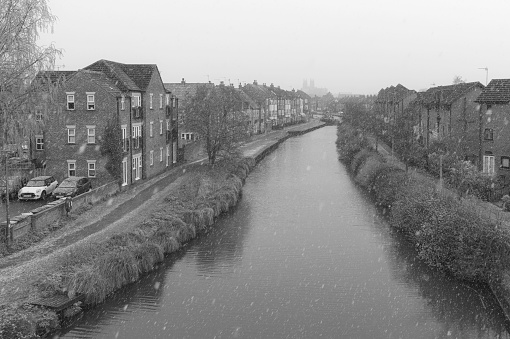 Beverley, UK - April 11, 2021: Snow falls in spring over the beck flanked by town houses on a bleak morning on April 11, 2021 in Beverley, Yorkshire, UK.