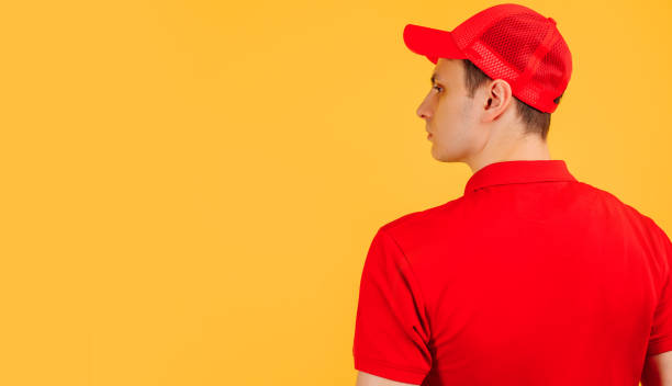 istock Rear view, courier wearing red uniform posing on yellow studio background 1312445760