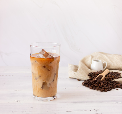 A glass cup with cold coffee and ice, coffee beans on a light background.