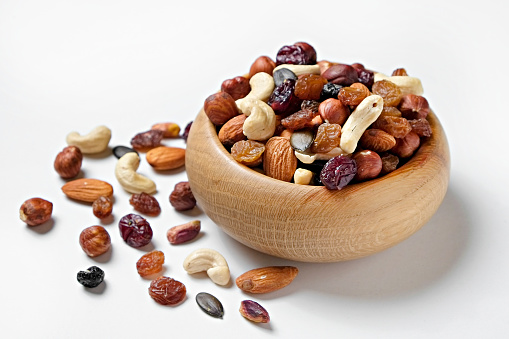Different types of nuts in a wooden bowl and scattered on isolated white background. Nutrient dense vegan snacks. Clean eating concept. Close up, copy space for text, top view, flat lay.