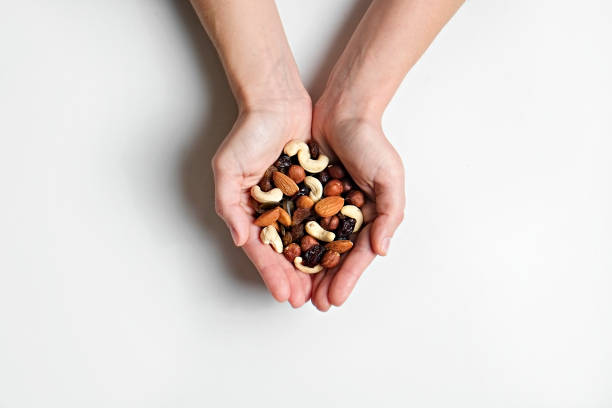 Bunch of different nuts on white table. Cropped shot of woman's hands holding a pile of mixed nuts and dried berries over isolated white background. Healthy high-calorie vegan food concept. Close up, copy space, top view, flat lay. cashew photos stock pictures, royalty-free photos & images