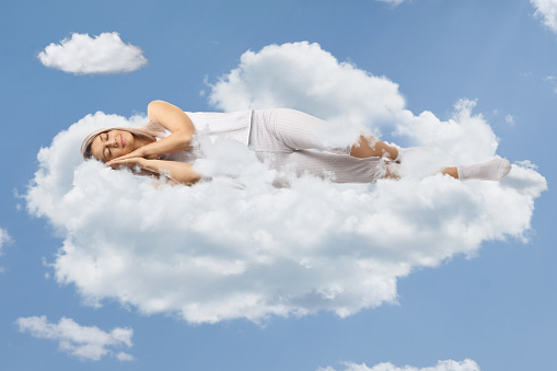 Young woman in pajamas sleeping on clouds and blue sky