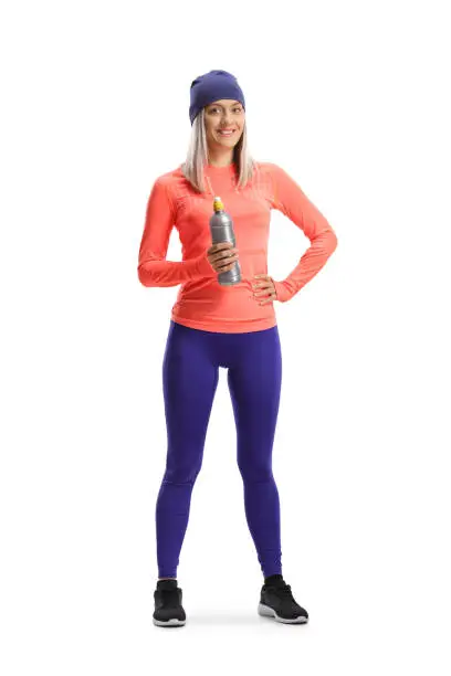 Full length portrait of a woman in running clothes and a hat holding a bottle isolated on white background