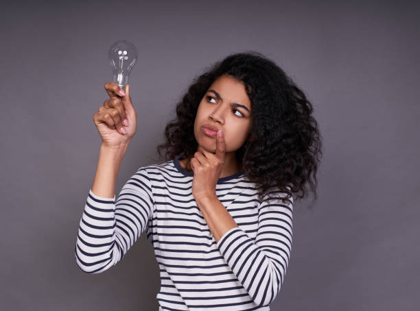 istock Thinking doubting young african lady with a light bulb in her hand. 1312454196