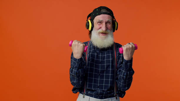 senior bärtigen mann musik hören über kopfhörer, trainieren, heben rosa hanteln, gesundheitswesen - weight training audio stock-fotos und bilder
