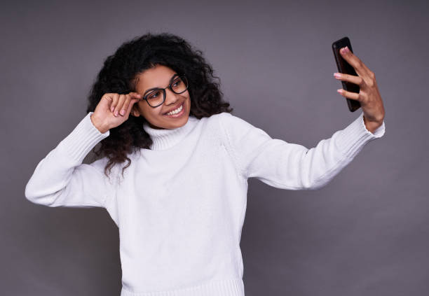 Beautiful dark-skinned girl takes a selfie on a gray background. stock photo