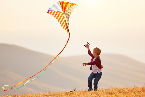 happy kid boy running with a kite at sunset outdoors