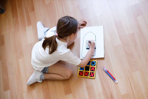 istock Little girl draws tic-tac-toe while sitting on the floor 1312456322