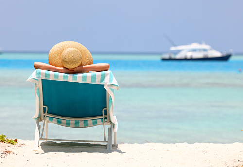 Back view of a female sunbathing in a hat on a sun lounger during a summer vacation on the beach by the ocean