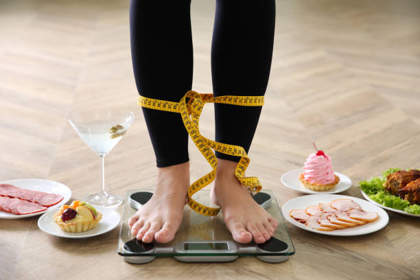 essen, alkohol nach den ferien und frau mit maßband stehen auf waage drinnen, nahaufnahme. übergewichtsproblem - bulimia stock-fotos und bilder