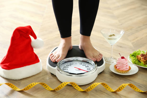 Food, alcohol left after Christmas holidays and woman with measuring tape standing on scales indoors, closeup. Overweight problem Food, alcohol left after Christmas holidays and woman with measuring tape standing on scales indoors, closeup. Overweight problem body conscious stock pictures, royalty-free photos & images