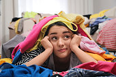 istock Pensive young woman with lots of clothes on floor in room. Fast fashion 1312459006