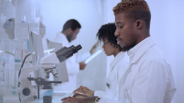 istock African ethnicity doctor using microscope in laboratory. Team in background 1312459153