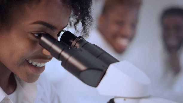 scienziati di etnia africana negli interni moderni del laboratorio. divertirsi mentre si lavora al microscopio - healthcare and medicine smiling group of people lab coat foto e immagini stock