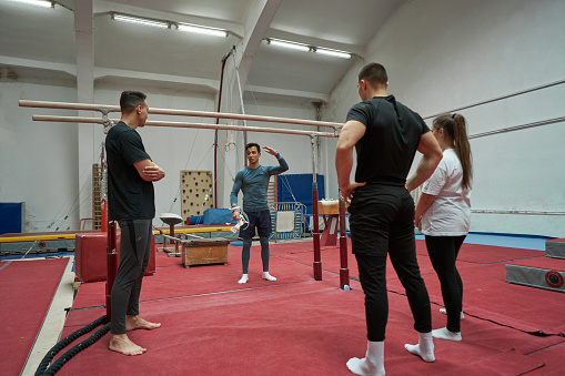 Gymnastic coach, explaining and showing off, his technique on the parallel bars, to his new members of a gymnastic club