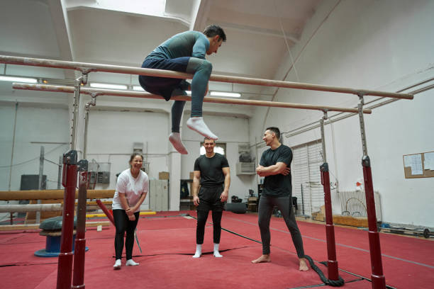 istock Gymnastic coach demonstrates the routine on the parallel bars, to new members 1312462113