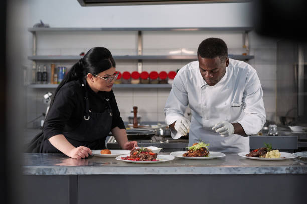 istock Female assistant, observing how her Jamaican chef decorating plate with a dish, learning the new technique 1312465395