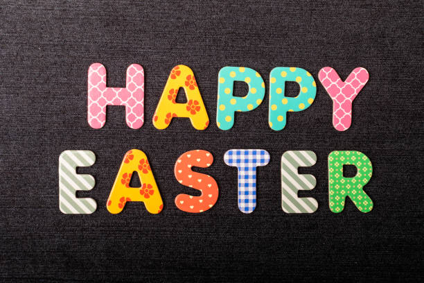 istock Card with Happy Easter words made from mixed vivid colored wooden letters on a textured dark black textile material that can be used as a message 1312465599