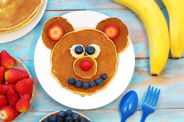 istock Fun idea for kids breakfast. Bear shaped pancakes with berries on blue wooden table, top view. Healthy food for children. Funny food for kids. 1312465676