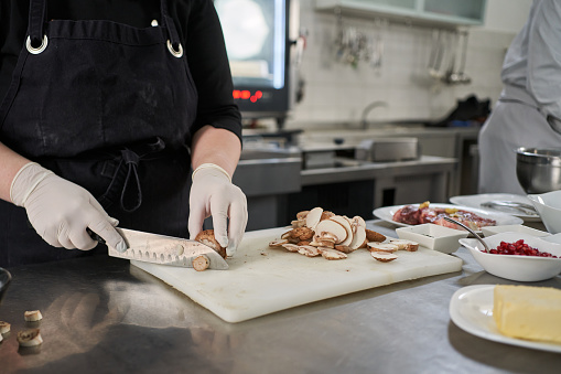 Dedicated young female chef, cutting the mushrooms on a cutting board in her modern commercial kitchen