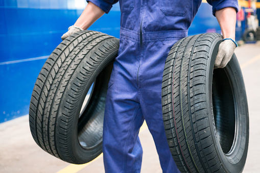 Car mechanic holding car tires in the auto repair shop. Close up of tires, unrecognizable person.